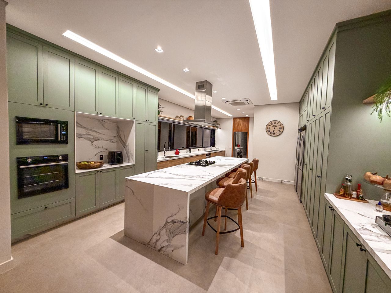 Cozinha com marcenaria verde-sálvia e ilha em mármore com banquetas de couro