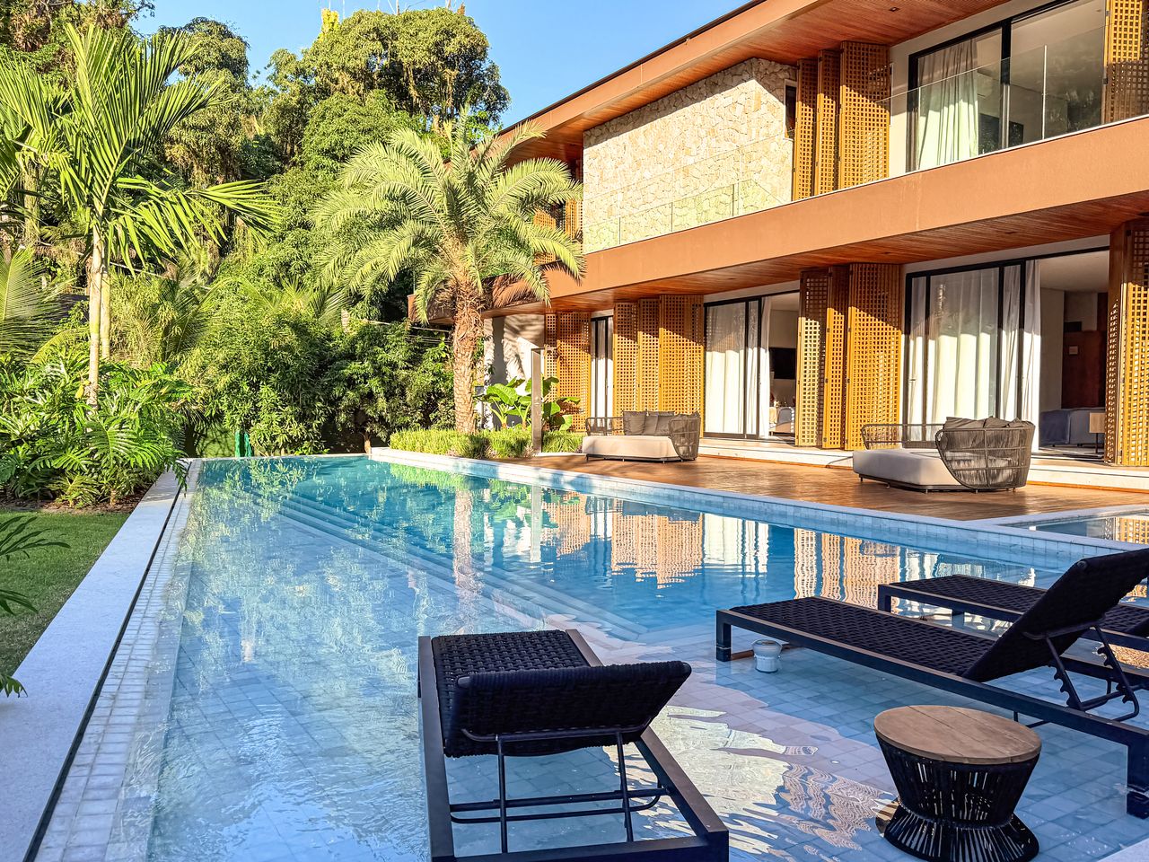 Fachada da residência integralmente revestida em muxarabi, com a piscina em primeiro plano ao entardecer